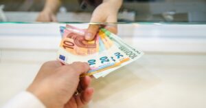 Ruke koje razmenjuju evre kroz staklo u menjačnici