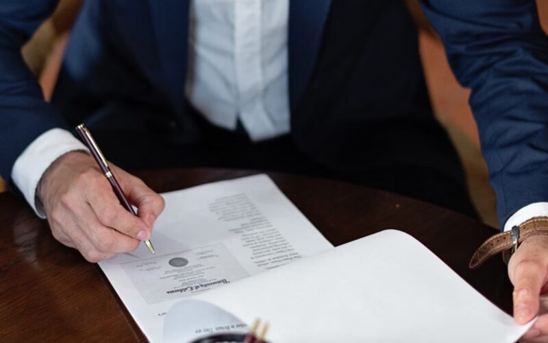 Muškarac u poslovnom odelu popunjava i potpisuje dokumentaciju za registraciju firme za radnim stolom